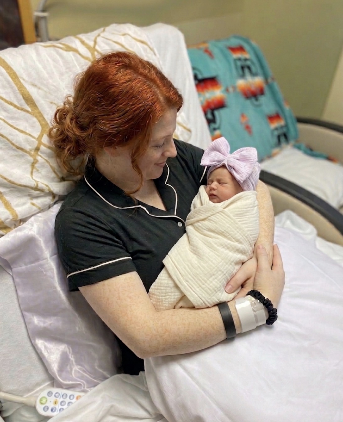 Mother holding her swaddled newborn baby in a hospital bed
